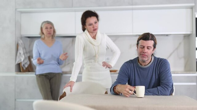 Elderly mother and woman scold swear at man. Male is upset because of family conflict, dejectedly listens to his wife and mother scolding him. Complex intergenerational relationships 