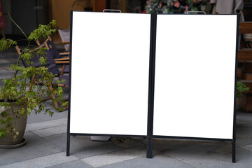 Two blank white outdoor advertising stand or sandwich boards mock up template placed by an outdoor dinning area of a restaurant.