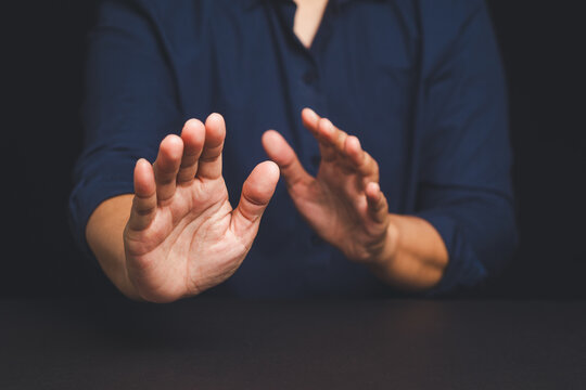 Man in navy shirt raising both hands in defensive stop gesture against dark background.