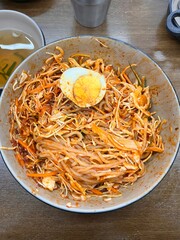 Bibimyeon, a flavorful Korean dish featuring cold noodles tossed in a spicy, tangy sauce, topped with fresh vegetables and a boiled egg. Perfect for summer meals, showcasing vibrant flavors and colors