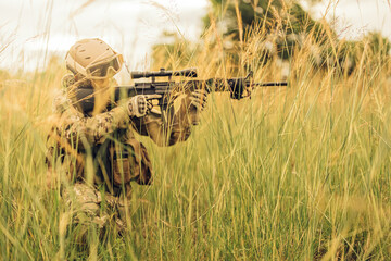 The soldier remains motionless, using the dense forest as cover while aiming his rifle toward an...