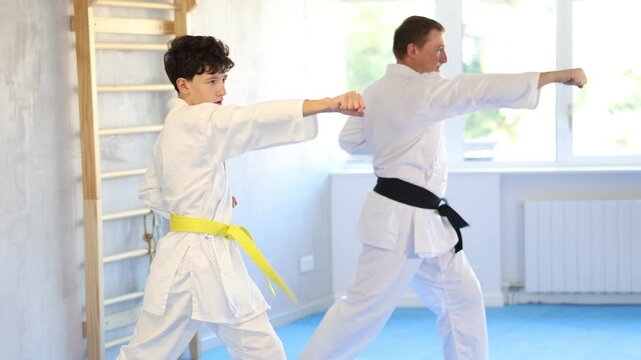 Adult man and boy teen karatekas train karate technique in studio