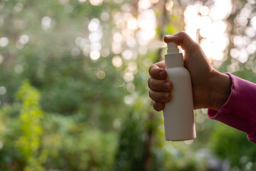 Person spraying insect repellent at her hand outdoors during summer. Trying to kill mosquitoes and flies. Clearly visible spray droplets. Prevention disinfection against mosquito bite during sunny day