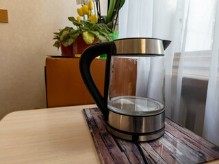 A glass teapot sitting on top of a wooden table next to a plant