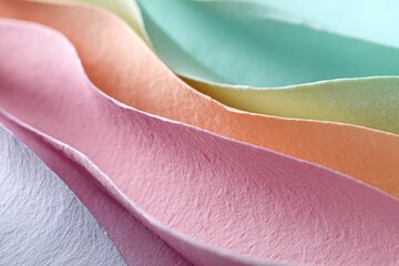 Softly torn pastel-colored paper is arranged in wave-like formations, casting gentle shadows and creating a textured surface that captivates the eye and inspires creativity