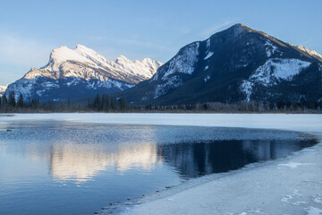 Snow-capped mountains reflect in a serene lake under clear sky in winter landscape