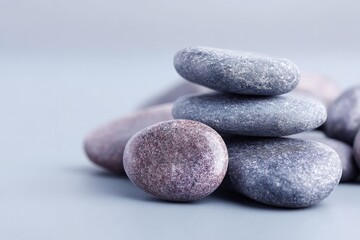 warm minimalistic image showing cluster of smooth dark hot stones for stone massage on light gray background