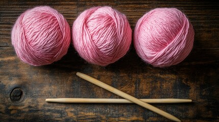 Pink yarn balls and knitting needles on a wooden surface