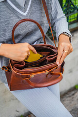 Stylish woman puts a yellow smartphone into a brown leather bag.