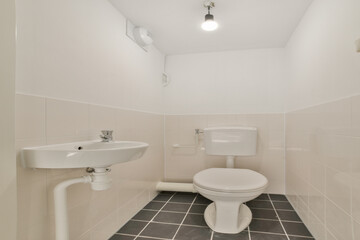 A clean, minimalist bathroom featuring a white wall-mounted sink and a modern toilet, complemented by sleek tiles and efficient lighting.