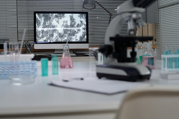 Detailed view of a laboratory setup with a microscope and computer analyzing specimens. Various laboratory equipment and chemicals are visible on countertops