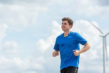Caucasian active sportsman running exercise at the wind turbine field.