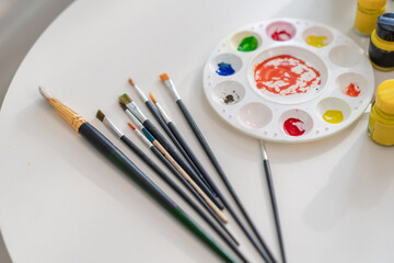 Colorful watercolor mixing plate and paintbrushes on white table. 