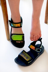 Barefoot girl sitting on chair wearing a fashion golden black sandals, white floor.