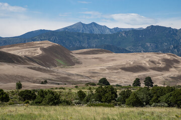 Desert landscape with sand dunes and mountains under a clear blue sky during daytime