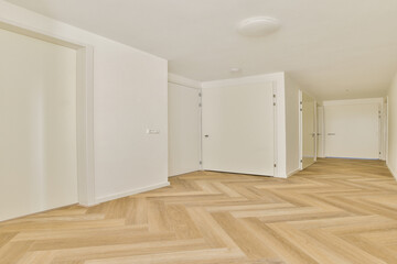 A spacious, well-lit modern hallway featuring stylish wooden herringbone flooring and minimalist white doors, creating an inviting atmosphere.