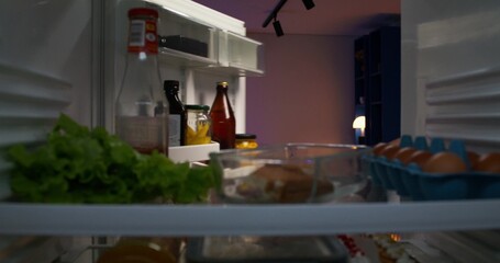 The man opens a bottle of beer standing near the refrigerator and starts drinking. He picks up the food container. View from the refrigerator