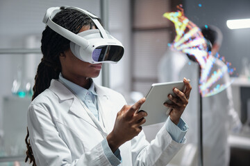Female scientist wearing VR headset and using tablet for conducting research in laboratory. DNA model visualization in background, creating tech-savvy working environment