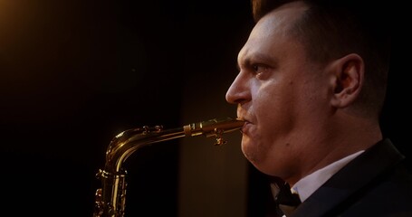 A stylish man plays the saxophone while standing on stage. Close-up of his face
