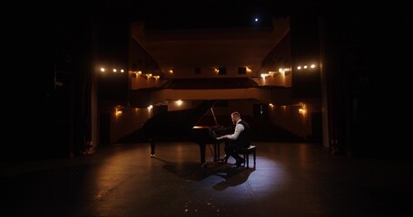 A concert rehearsal. A pianist plays the piano on a theater stage. The auditorium is empty. Dimmed...