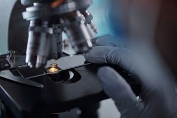 Gloved hands adjusting microscope in laboratory setting showing precision needed for scientific research and analysis