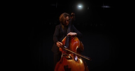 A man plays the double bass in the lamplight. He stands on the stage of the theater © m-art