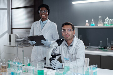 Portrait of two scientists conducting research in laboratory setting, with one looking at camera...