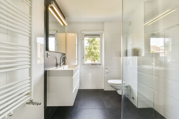 Elegant modern bathroom featuring sleek white tiles, a glass shower, and minimalist fixtures, enhancing a clean and spacious feel.