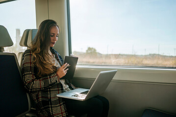 Businesswoman working on laptop and taking notes on train