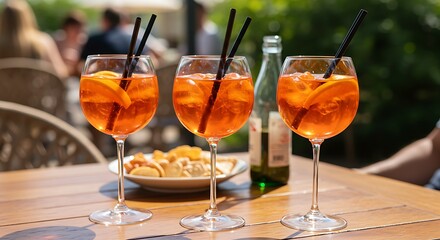 Vibrant orange cocktails with straws and orange slices are arranged on a wooden table, indicating a social aperitivo gathering outdoors