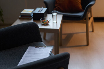 Clipboard with paper document lying on armchair against small square table with candies, glass of...