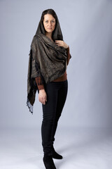 A  dark-haired woman wearing black pants, a brown top and a woven paisley shawl draped over her...