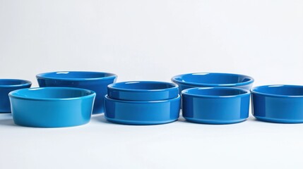 Group of small and large blue pet food bowls arranged in a row on white background.