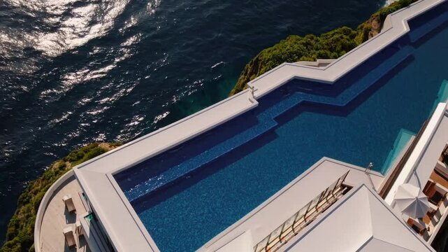 Aerial view of a luxury hotel with a striking blue infinity pool overlooking the ocean. Clear waters and tropical foliage surround the architectural design. 