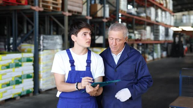 Young guy manager boss checks papers invoices together with elderly male employee and revise availability and quantity of goods in stock