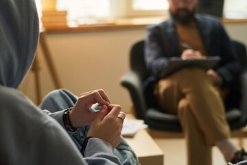 Hands of teenage girl wearing blue hoodie sitting in front of school psychologist during discussion...