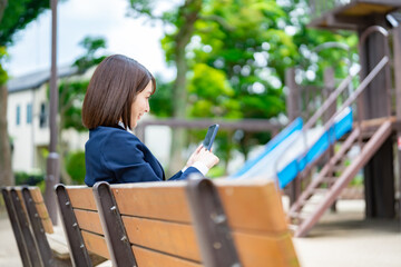 ベンチに座り携帯を持つ女子高生