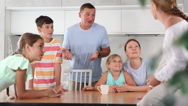 Friendly family gathered at table and cheerfully discuss past day. Mom, dad, three daughters and son solve important issue in friendly atmosphere