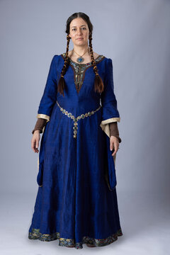 A Medieval woman wearing a blue silk gown called a bliaut. She has long, dark hair arranged into plaits. 