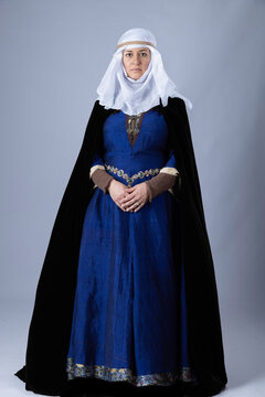A Medieval woman wearing a blue silk gown called a bliaut. She has long, dark hair arranged into plaits. 