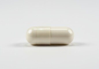 Close up of a single white capsule pill laying horizontally on a bright white surface in studio shot