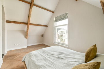 A stylish modern bedroom featuring exposed wooden beams, a large window for natural light, and...