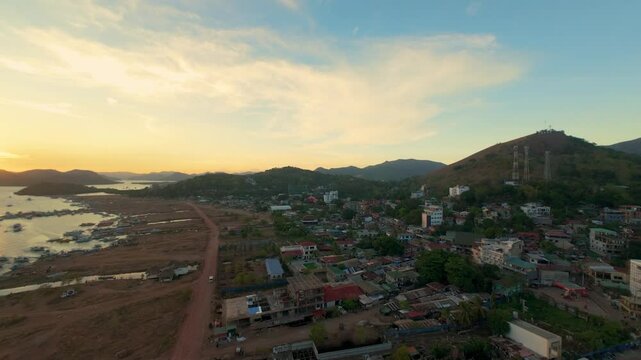 Sunset aerial view over Coron town and bay with Mount Tapyas hillside antennas harbor flats rooftops and warm sky in Palawan