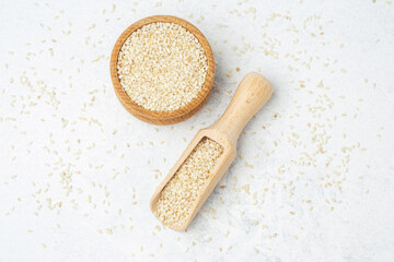 Sesame seeds in wooden bowl and scoop on light background