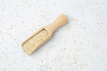 Sesame seeds in wooden scoop on light background with scattered seeds