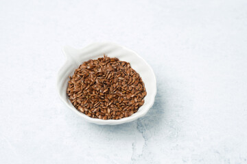 Brown flax seeds in a ceramic bowl on a light background for healthy recipes