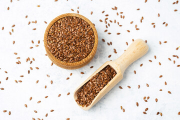 Brown flaxseeds in wooden bowl and scoop on white background