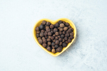 Whole allspice berries in heart-shaped bowl on light background