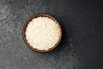 Quality white rice in a rustic bowl on a textured black surface