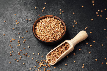 Unique buckwheat groats in a bowl with wooden scoop on dark background